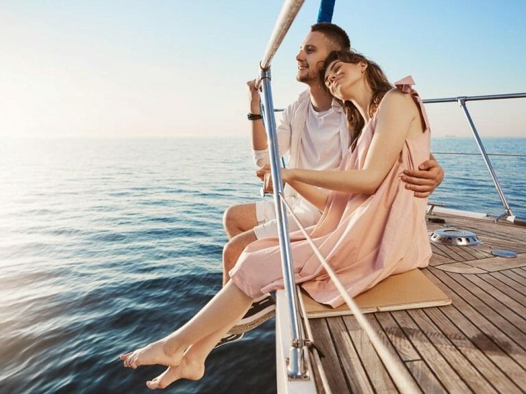 Happy beautiful adult couple sitting on side of yacht, watching at seaside and hugging while on vacation. Tan might fade but such memories you share with one you love, last forever